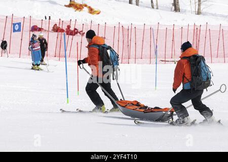 KAMCHATKA, RUSSIA, MARCH 28, 2019: Rescuers Kamchatka Rescue Squad on alpine ski with stretcher skiing down mount slope for first medical aid, evacuat Stock Photo