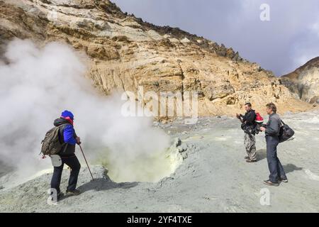 Group tourists watching eruption of hot springs, fumes fumarole, volcanic gas-steam activity in crater active volcano, beautiful mountain landscape. K Stock Photo