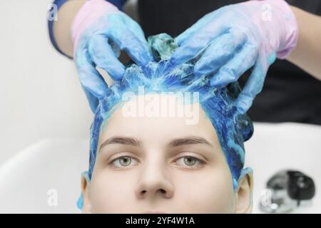 Hairstylist hands in gloves washing hair with shampoo and conditioner in professional beauty salon. Close-up view of head young woman with blue hair a Stock Photo