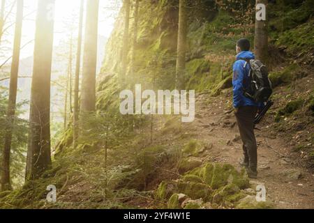 A guy tourist with a backpack stands on a mountain trail and looks into the distance. The concept of travel and adventure. Traveler Man with backpack Stock Photo
