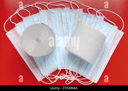 Top view of rolls toilet paper on background antiviral face masks and red color backdrop. World pandemic insurance, coronavirus, airborne diseases and Stock Photo