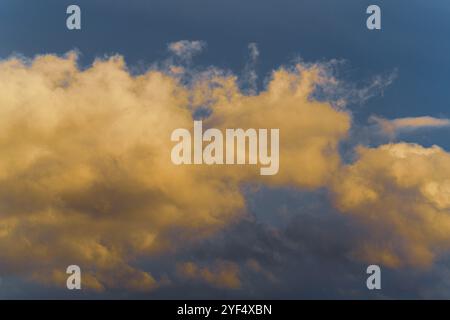 Stunning fluffy thunderstorm clouds illuminated by disappearing rays at sunset and dark cumulonimbus floating across sunny blue sky to change season w Stock Photo