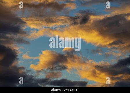 Dramatic fluffy clouds illuminated by disappearing rays at sunset, dark thunderclouds floating across blue sky to weather change. Amazing view of natu Stock Photo