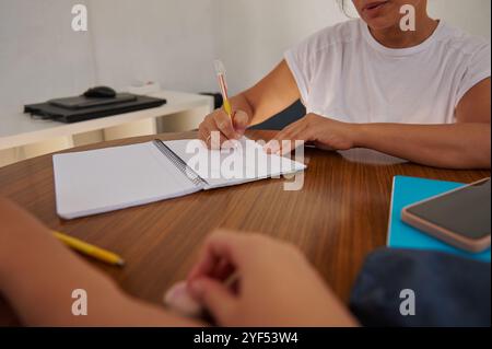 Two individuals are engaged in a writing task at a wooden table, focused on taking notes. This image conveys collaboration, education, and productivit Stock Photo