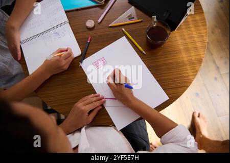 Top view of two students working on homework at a round table, with notebooks, pencils, and coffee. Collaborative learning setting. Stock Photo