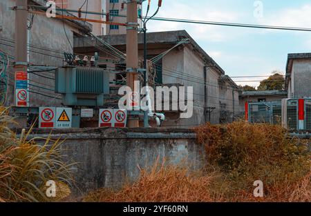 Industrial power station with multiple warning signs, electrical transformers, and exposed cables in an urban setting Stock Photo