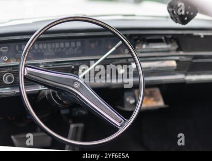 A close-up of a vintage car's steering wheel, with a fuzzy dice hanging from the rearview mirro Stock Photo