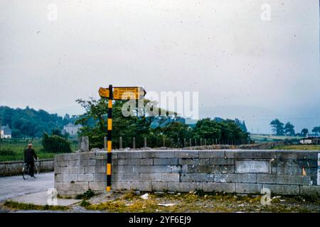 A man cycling past a junction in Castleisland, County Kerry, Ireland in 1957 with an old sign showing directions for Castlegregory, Dingle and Tralee. Stock Photo