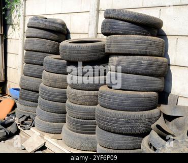 A pile of old and used vehicle tyres stacked against a cement wall outside a garage. Stock Photo