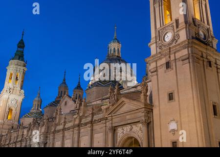 Illuminated Basilica del Pilar in Zaragoza, Spain, at dusk, with serene reflections on the Ebro River. Ideal for travel, architecture, and cultural th Stock Photo