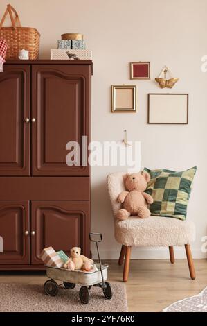 Blank picture frames hanging next to a cupboard in a room with teddy bears sitting on a chair and in a wagon Stock Photo