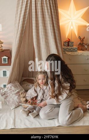 Happy mother and daughter sitting in a play teepee in a bedroom reading a book together Stock Photo