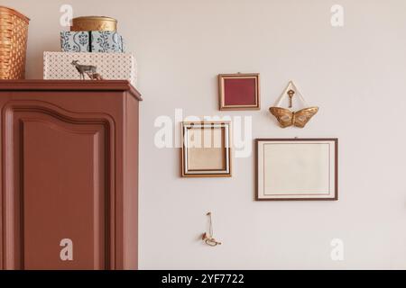 Blank picture frames hanging on a wall next to assorted boxes, containers and baskets on top of a cupboard Stock Photo