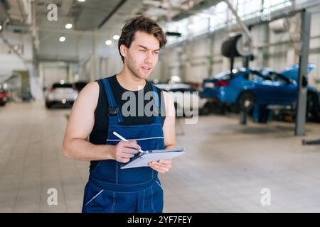 Vertical portrait of serious auto mechanic male checking car with tablet in garage car service. Professional technician male repairing vehicle at Stock Photo