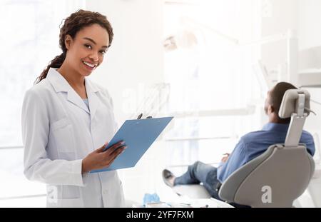 Smiling female dentist filling medical form in cabinet Stock Photo