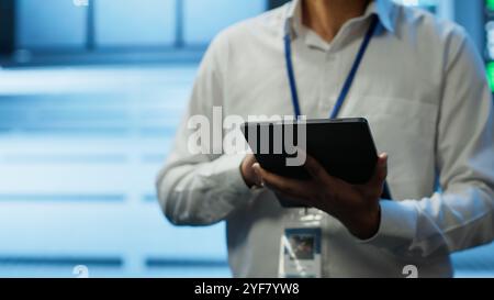 Software developer walking in data center, managing and maintaining databases, ensuring data integrity and security. Close up of man updating server room mainframe systems using tablet, camera A Stock Photo