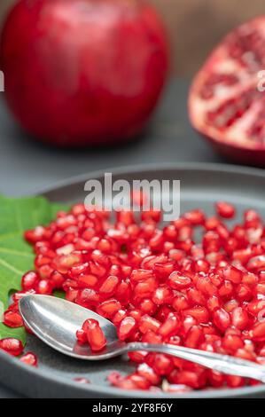 Pomegranate seeds and a spoon in front of a whole pomegranate fruit as well as one sliced in half. Stock Photo