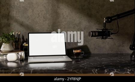 A modern freelance podcaster office workspace featuring a laptop with a white screen mockup, headphones, and a microphone on a black marble table agai Stock Photo