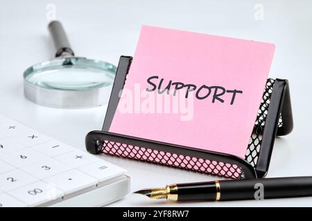 Business concept. The phrase, the text, the words SUPPORT are written on a pink sticker on a black stand on a gray background. Stock Photo