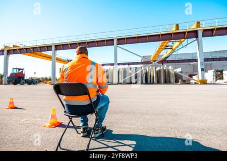 Male engineer worker in safety vest sitting, feeling tired from work hard at factory Stock Photo
