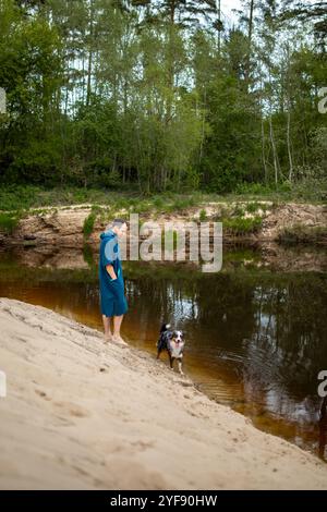 Man in Teal Poncho Standing by the River, Dog Playing by the Riverside Stock Photo