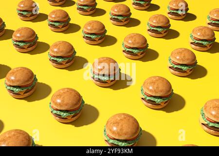 Many delicious burgers forming a repetitive pattern on a vibrant yellow backdrop, creating a visually appealing image ideal for food and restaurant th Stock Photo