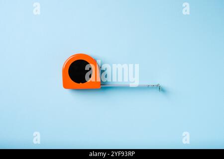 Orange retractable tape measure on blue background Stock Photo