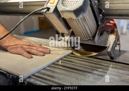 close-up of skilled worker cutting ceramic tile with professional tile cutter on construction site Stock Photo
