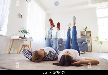 Young happy relaxed family couple holding legs up pose to rest, lying on floor enjoying carefree Stock Photo