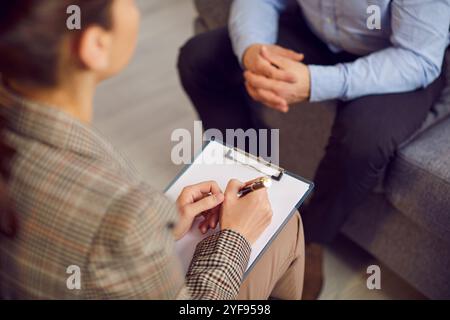 Woman therapist with a clipboard talking to a male patient during a psychotherapy session Stock Photo
