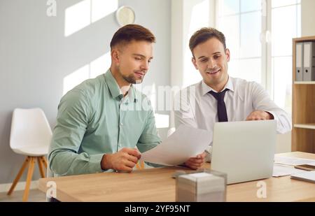 Two male colleagues are discussing documents at work meeting in bright office. Stock Photo