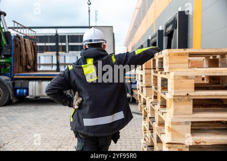 Worker in Safety Gear Directing Forklift Operations at an Industrial Freight Area with Pallets Stock Photo