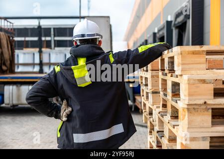 Worker in Safety Gear Directing Forklift Operations at an Industrial Freight Area with Pallets Stock Photo