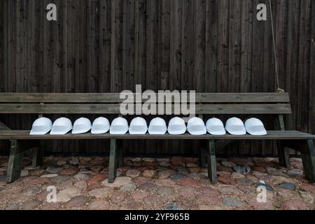 Row of White Safety Helmets Lined Up on a Wooden Bench Against a Dark Timber Background Stock Photo