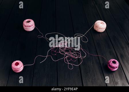 Tangled multicolored threads from four skeins lie on black wooden boards. Threads for knitting on a black background. Stock Photo