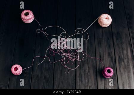 Tangled multicolored threads from four skeins lie on black wooden boards. Threads for knitting on a black background. Stock Photo