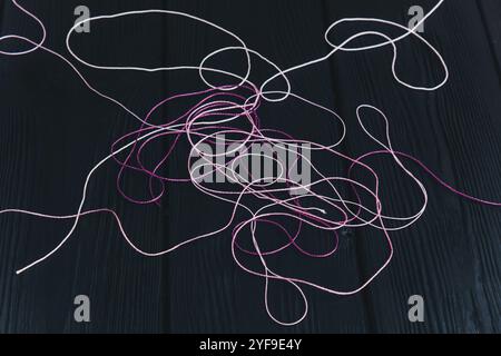 Tangled multi-colored threads lie on black wooden boards. Threads for knitting on a black background. Stock Photo