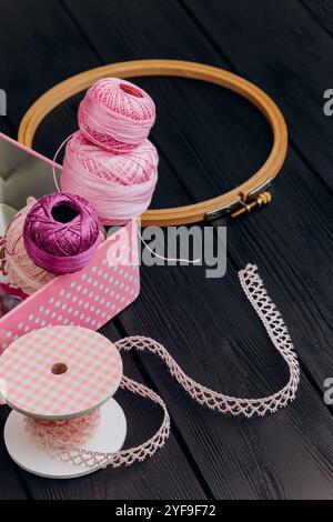 Assorted yarn and sewing tools in a pink tin box on a black wooden background create a visually appealing arrangement for craft lovers. Stock Photo