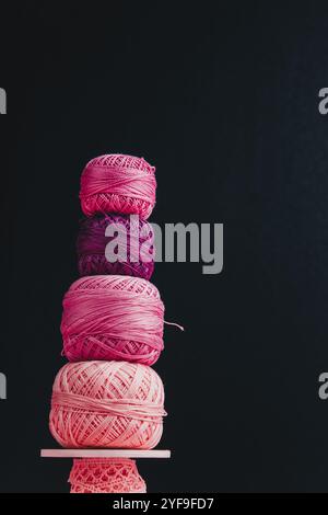 A collection of knitting skeins stacked on top of each other on a pastel pink wooden surface with a black background behind. Stock Photo