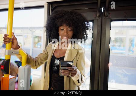 Afro woman using smart phone while standing in bus Stock Photo
