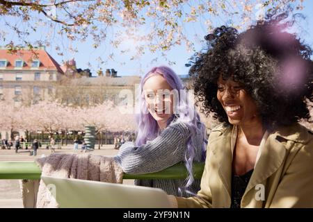 Happy multiracial female friends using laptop in park at sunny day Stock Photo