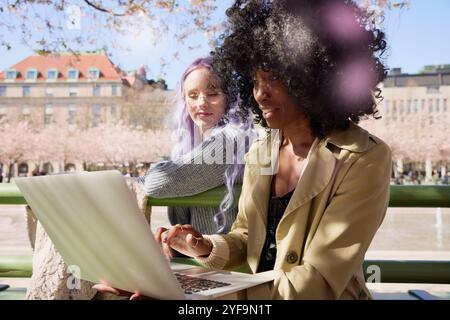 Curly haired woman using laptop with female friend at street Stock Photo