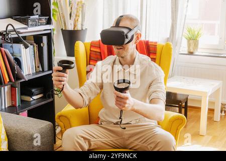 Mid adult man wearing virtual reality headset while playing video game at home Stock Photo