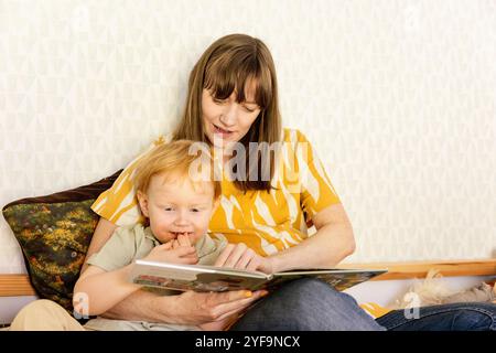 Mother and son reading book while sitting on bed at home Stock Photo