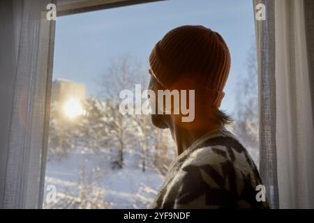 Side view of man wearing beanie while looking through window at home Stock Photo
