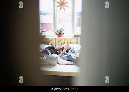 Siblings using smart phone while lying on bed at home Stock Photo