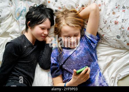 Directly above shot of brother and non-binary sibling using smart phone while lying on bed at home Stock Photo