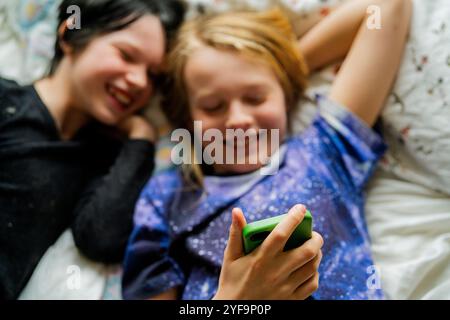 Smiling girl using smart phone with brother while lying on bed at home Stock Photo