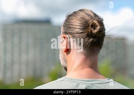 Rear view of man in hair bun wearing hearing aid device Stock Photo