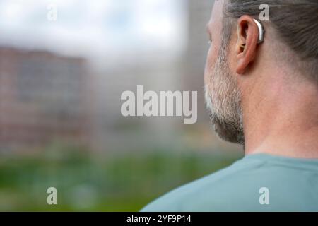 Rear view of man with gray beard wearing hearing aid device Stock Photo